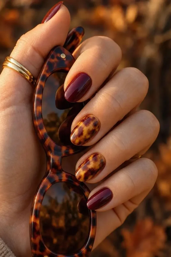 Oval nails with a tortoiseshell pattern in amber and dark burgundy tones next to solid burgundy nails